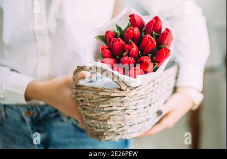 florist woman holding a basket with red tulips in white paper. flower shop delivery concept Stock Photo