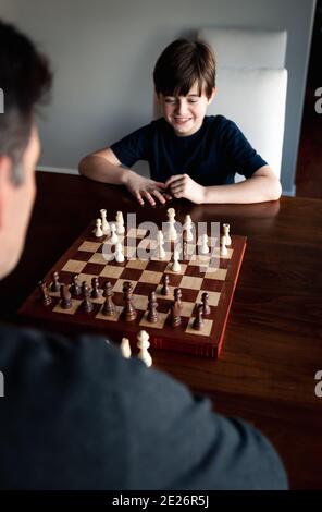 Father and son sitting at a table indoors playing a game of chess. Stock Photo
