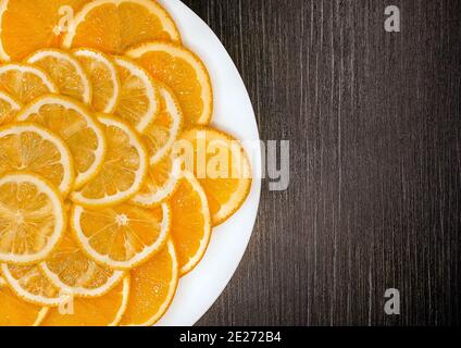 Sliced orange and lemon in a white plate on a dark wooden texture background, copy space. Stock Photo