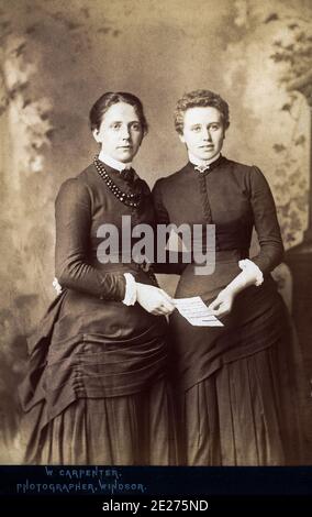 Two fashionably dressed Victorian women from the 1880s, possibly sisters, look happy to have received a letter. Stock Photo