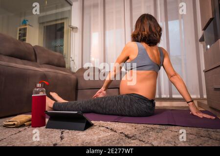 Young caucasian pregnant female stretching and doing yoga indoors Stock Photo