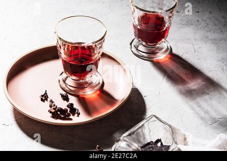 Refreshing fruit herbal tea in glasses, ripe pomegranate on plate, hibiscus tea and dry rose petals, hard light with harsh shadows
