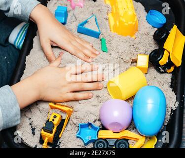 Child playing with kinetic sand and toy construction machinery. Hand of child in sand close up. Flat lay, top view. Indoor Table Game. Creativity Game Stock Photo