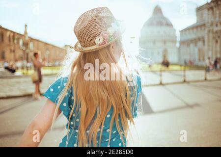 Seen from behind trendy girl in blue overall and hat exploring attractions near Pisa Cathedral. Stock Photo