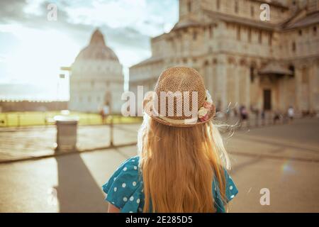 Seen from behind modern girl in blue overall and hat sightseeing near Pisa Cathedral. Stock Photo