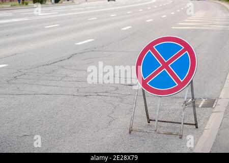 Round red cross on blue background sign against cracked asphalt background. Traffic sign meaning that it is not allowed to park vehicles here. Stock Photo