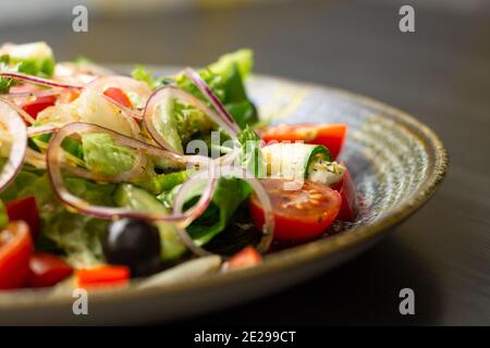 Vegetable salad with greens and olives in dark clay plate on wooden table Stock Photo
