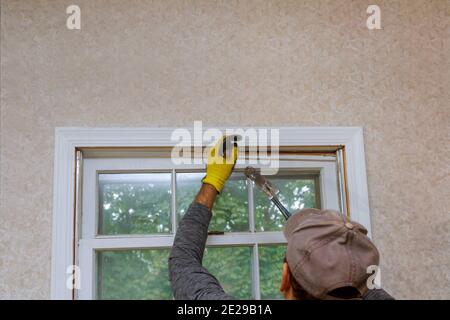 A carpenter with process of removing an old wooden window from an opening in a house before replacing it with a new one. Stock Photo