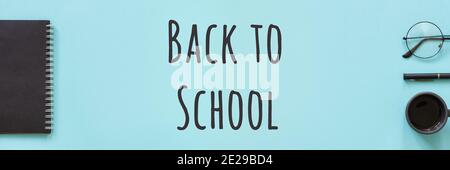 Back to school text and office supplies, stationery. Black color notepad, cup of coffee, spectacles and pen on blue background. Concept education. Fla Stock Photo