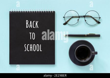 Back to school text and office supplies, stationery. Black color notepad, cup of coffee, spectacles and pen on blue background. Concept education. Fla Stock Photo