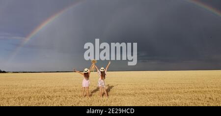 In a wheat field after the rain, two girls run. Colorful real rainbow over the horizon. europe Ukraine. Summer crop fields, ripening wheat field. Stock Photo