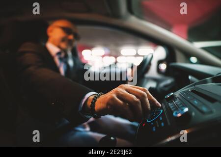 Mature businessman in suit is adjusting a volume on his stereo while driving a car. Stock Photo