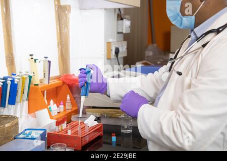 Indian medical scientist doctor wearing surgical face mask doing Chemical or drug research in clinical laboratory for covid virus vaccine, healthcare Stock Photo