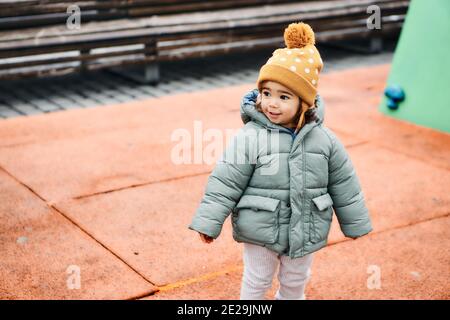 Shallow focus closeup of a female kid wearing winter clothes while standing on the playgrou Stock Photo