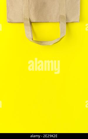 Brown paper bag with handles on Yellow Background. Eco reusable shopping bag for groceries, gifts, goodies. Shopping concept Stock Photo