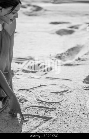 black and white image of a beautiful young African woman writing i love you on the sand with her finger Stock Photo