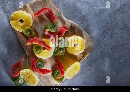 Dried fruits: Yellow candied pineapple rings, red papaya and green on a wooden cutting board on gray concrete Stock Photo