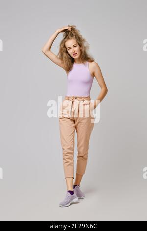 Pretty girl with blonde messy hair in tank top and trousers lifting hair