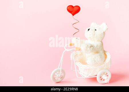 White bear on a bicycle holding a heart on a pink background with copy space Stock Photo