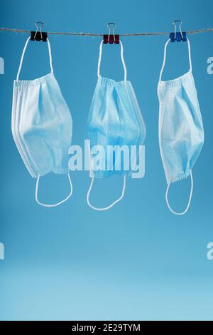 Three surgical masks hang on a clothesline against a blue background. Free space Stock Photo