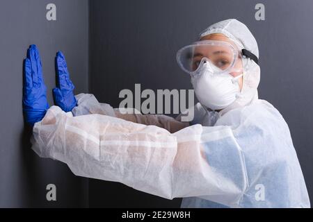 A doctor in uniform, pressing his hands against a gray wall, looks at the camera. Fatigue while dealing with coronavirus. Stock Photo