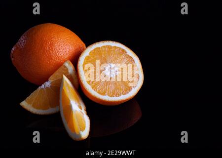 Ripe orange fruit sliced coposition on a black reflective background Stock Photo