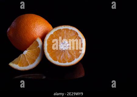 Ripe orange fruit sliced coposition on a black reflective background Stock Photo