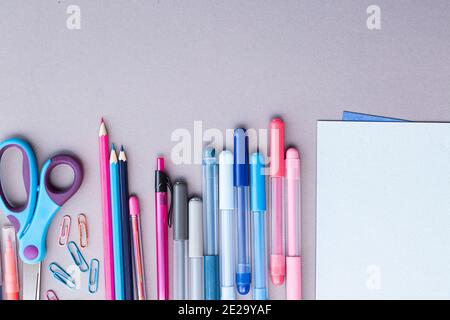Various stationery in pink and blue colors, blank sheets of paper, on a gray background with copy space. Flat lay with pencils, scissors, pens, paper Stock Photo