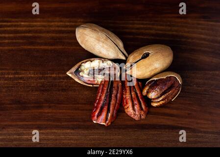 Pecan nuts on a wooden table. Heap or stack of pecan. Cracked and opened pecan nuts and nuts in shell. Stock Photo