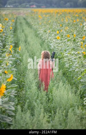 A woman with a camera on a green road leading through fields of sunflowers. Poland. Warsaw Stock Photo