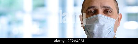 Close-up portrait of swarthy man wearing disposable protective medical face mask on blurred hospital background. Banner. Concept of the danger of viru Stock Photo