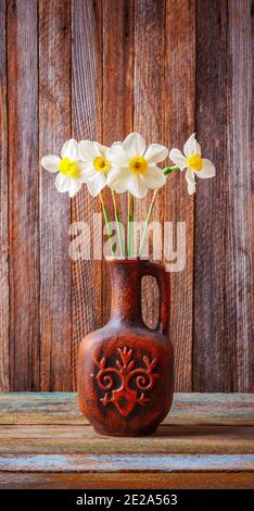 still life of a bouquet of daffodils flowers in an old ceramic jug on a wooden vintage grunge background closeup Stock Photo