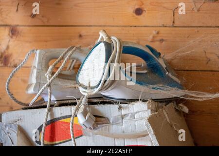 two old irons with cobwebs abandoned on an anonymous old and broken cardboard box Stock Photo