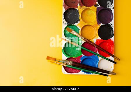 Used Acrylic Colours and Brushes. Palette placed on yellow Coloured Board, Top Angle View, Studio Shot Stock Photo