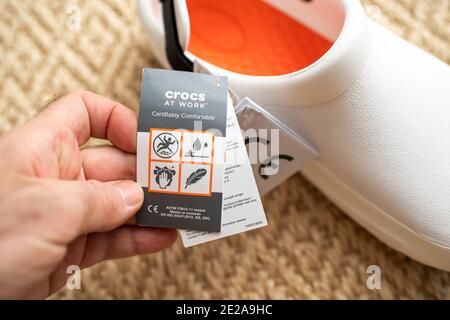 Paris, France - Dec 13, 2020: POV male hand holding paper advertising tag of Crocs at work comfortable shoes with price tag etiquette with instructions for use pictograms Stock Photo