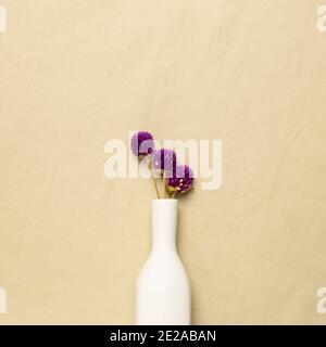 Vase of purple globe amaranth flowers on beige fabric background. flat lay, top view, copy space Stock Photo