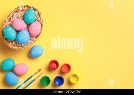 Happy easter. Multi-colored eggs in a basket, brushes and paints on a yellow background. Flat lay greeting card with copy space. Stock Photo