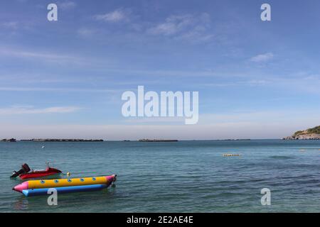 Picture of the view of the sea and sky. There are red scooter boat and yellow banana boat in the foreground. Stock Photo