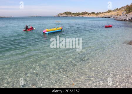 Picture of the view of the sea and sky. There are red scooter boat and yellow banana boat in the foreground. And mountains in the background. Stock Photo