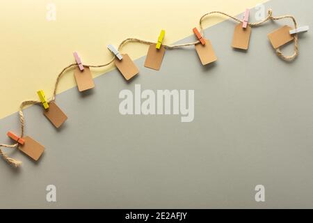 Paper tags tied with colored clothespins to jute rope, rope with tags on trendy yellow gray background Stock Photo