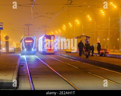 Moscow.Russia. December 26, 2019. Trams in the fog lit by a network of LEDs arrive at a bus stop with passengers. Environmentally friendly public Stock Photo