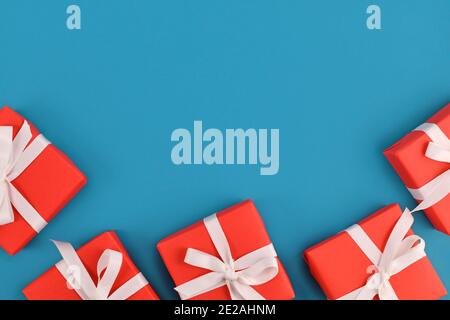 Small red gift boxes with white ribbons at bottom of blue background with empty copy space Stock Photo