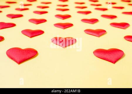 A lot of identical red silk hearts lying staggered on a yellow background. Symbol of love, tenderness and passion.