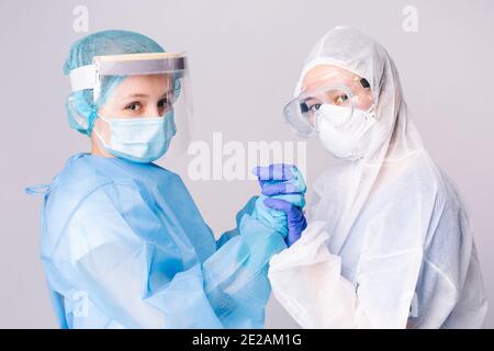 Pandemic. Tired doctors in covid-19 protective gear hold hands in support of a dire situation. Gray background. Stock Photo