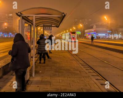 Moscow.Russia. December 26, 2019. Trams in the fog lit by a network of LEDs arrive at a bus stop with passengers. Environmentally friendly public Stock Photo