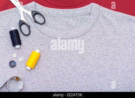 Simply composition with buttons, tape measure, scissors, spool of thread. Sewing equipment on gray t-shirt, lay out, top view. Stock Photo