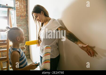 Young cheerful family doing apartment repair together themselves. Happy mother and son doing home makeover or renovation. Concept of relations, moving, love. Measuring before painting Stock Photo