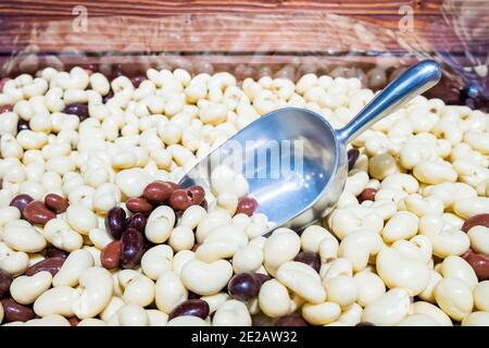 Aluminum scoop in a scattering of round white and brown dragees on a store counter. Delicious and healthy sweets made from nuts coated with chocolate. Stock Photo