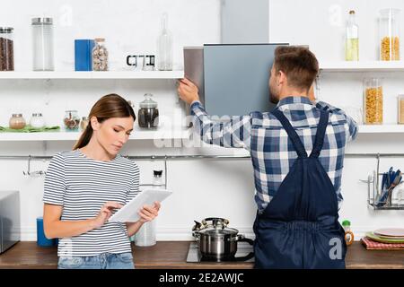 young woman using tablet near handyman repairing extractor fan in kitchen Stock Photo