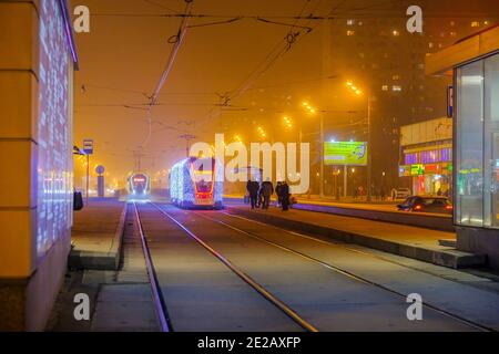 Moscow.Russia. December 26, 2019. Trams in the fog lit by a network of LEDs arrive at a bus stop with passengers. Environmentally friendly public Stock Photo